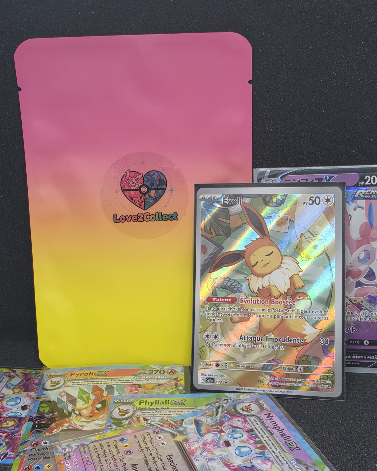 Pochette à thème évoli de chez Love2Collect. On y vois la pochette en fond et plusieurs autre cartes Pokémon